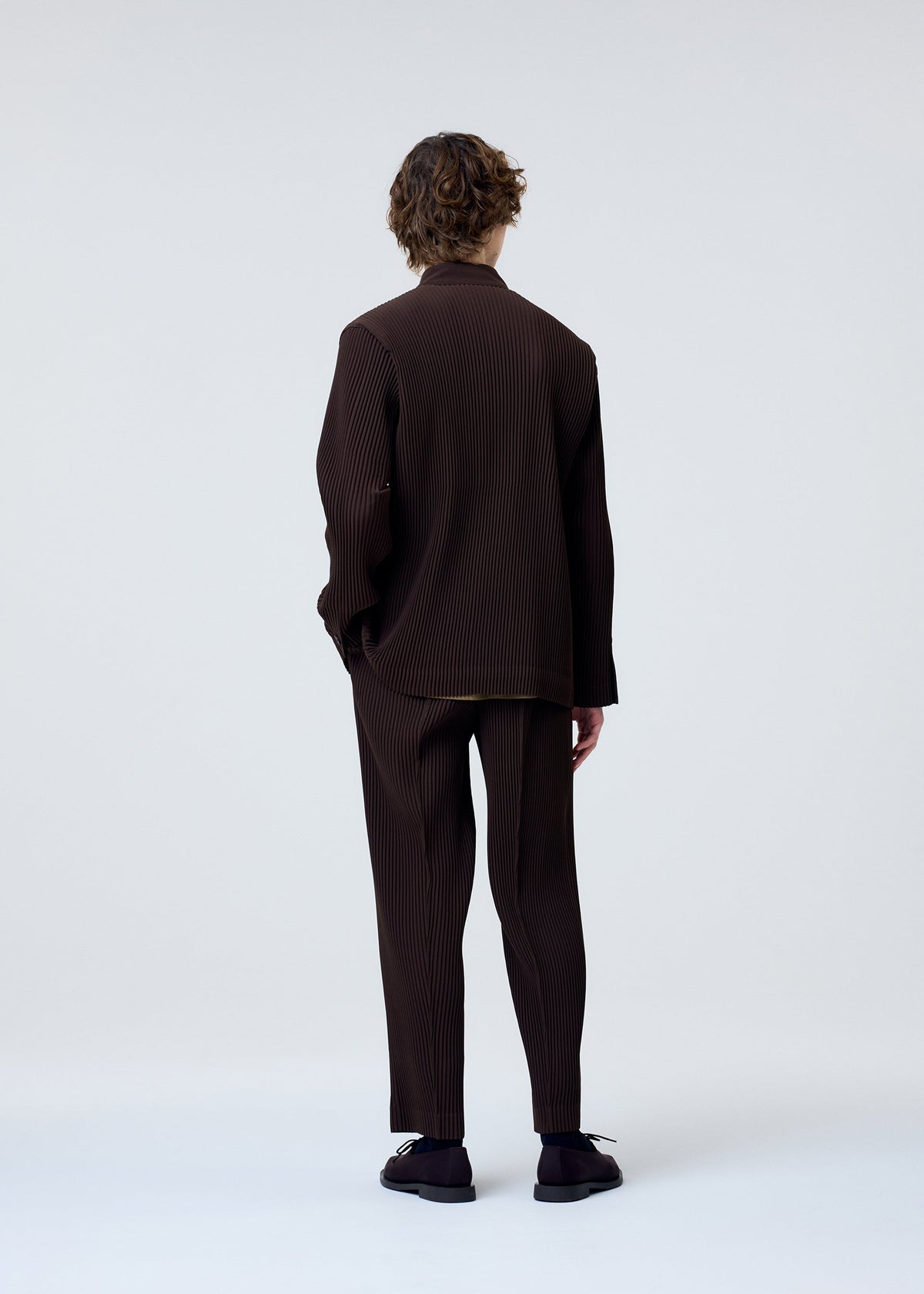 A model wears the HOMME PLISSÉ ISSEY MIYAKE TUXEDO PLEATS trousers.