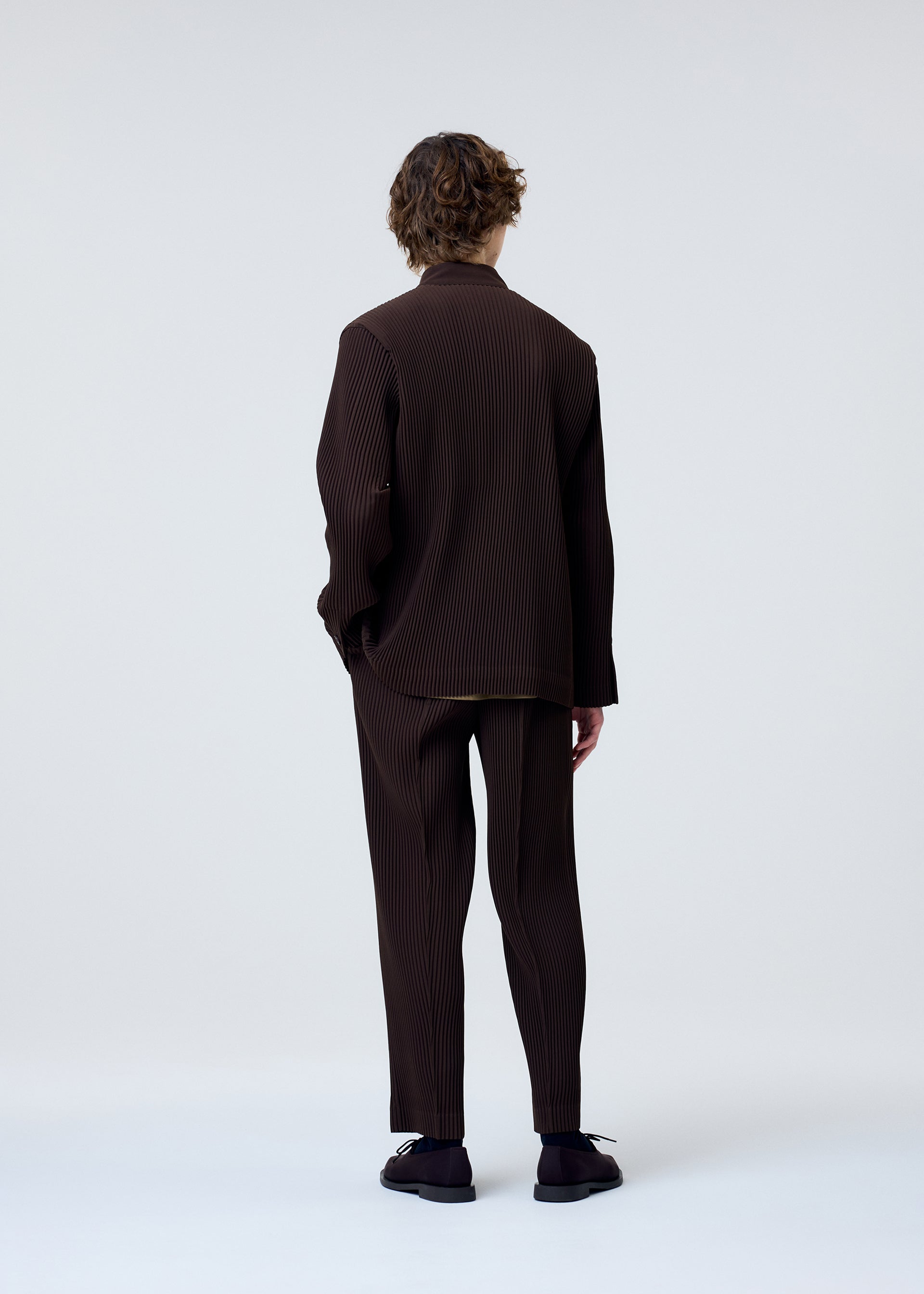 A model wears the HOMME PLISSÉ ISSEY MIYAKE TUXEDO PLEATS trousers.
