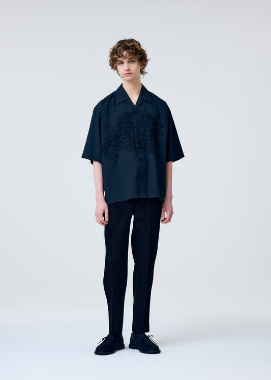 A model wears the HOMME PLISSÉ ISSEY MIYAKE EMBROIDERY PRESS SHIRT shirt.