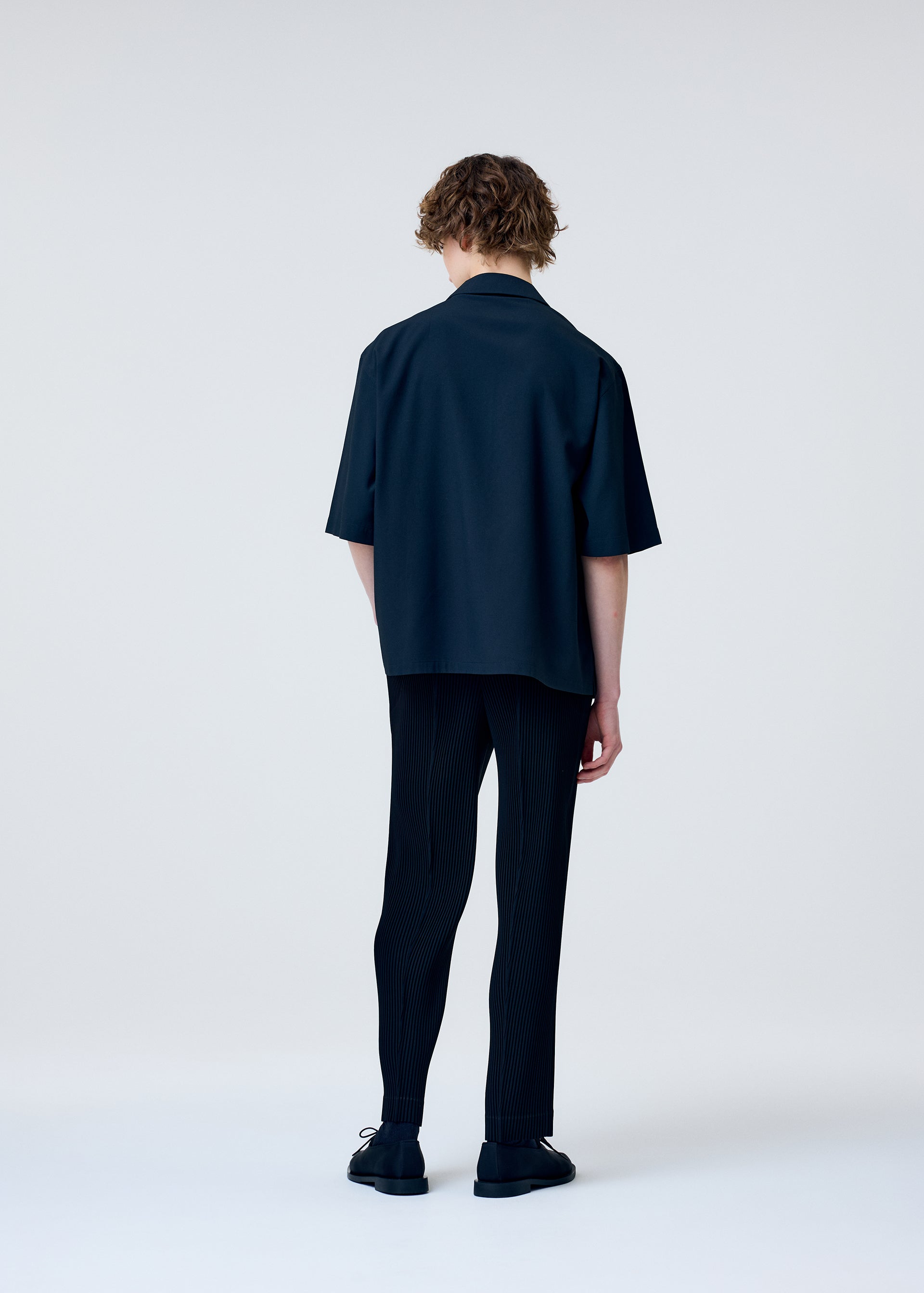 A model wears the HOMME PLISSÉ ISSEY MIYAKE EMBROIDERY PRESS SHIRT shirt.
