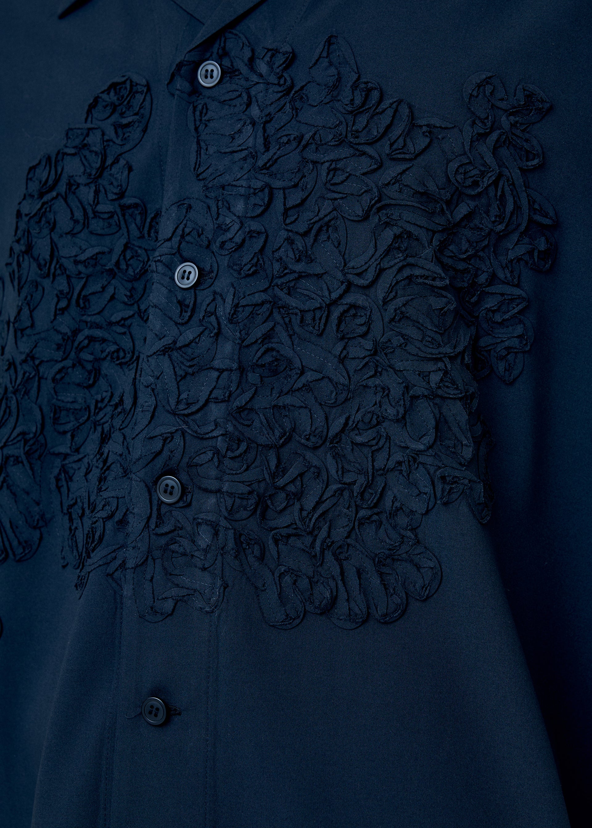 A model wears the HOMME PLISSÉ ISSEY MIYAKE EMBROIDERY PRESS SHIRT shirt.