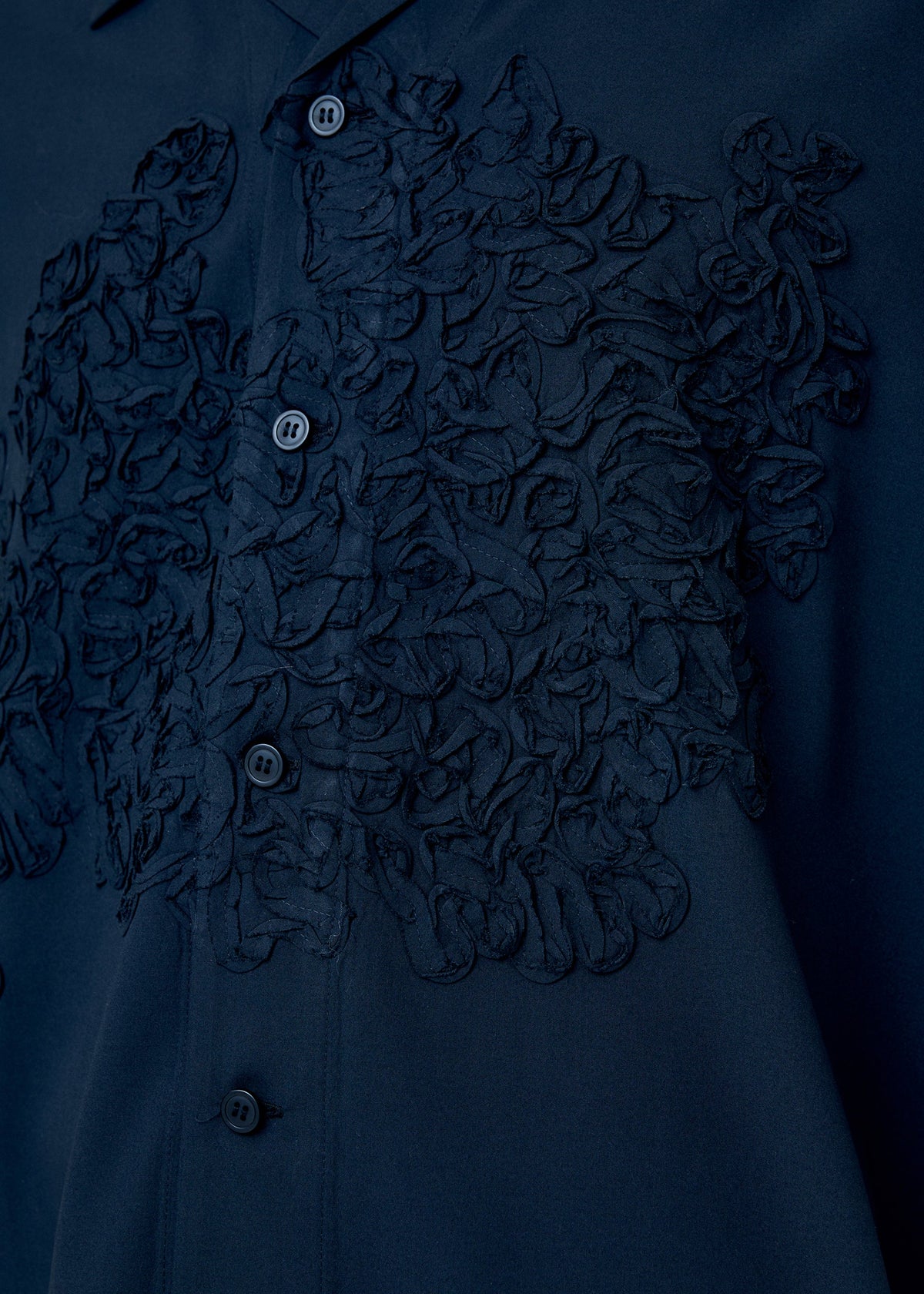 A model wears the HOMME PLISSÉ ISSEY MIYAKE EMBROIDERY PRESS SHIRT shirt.