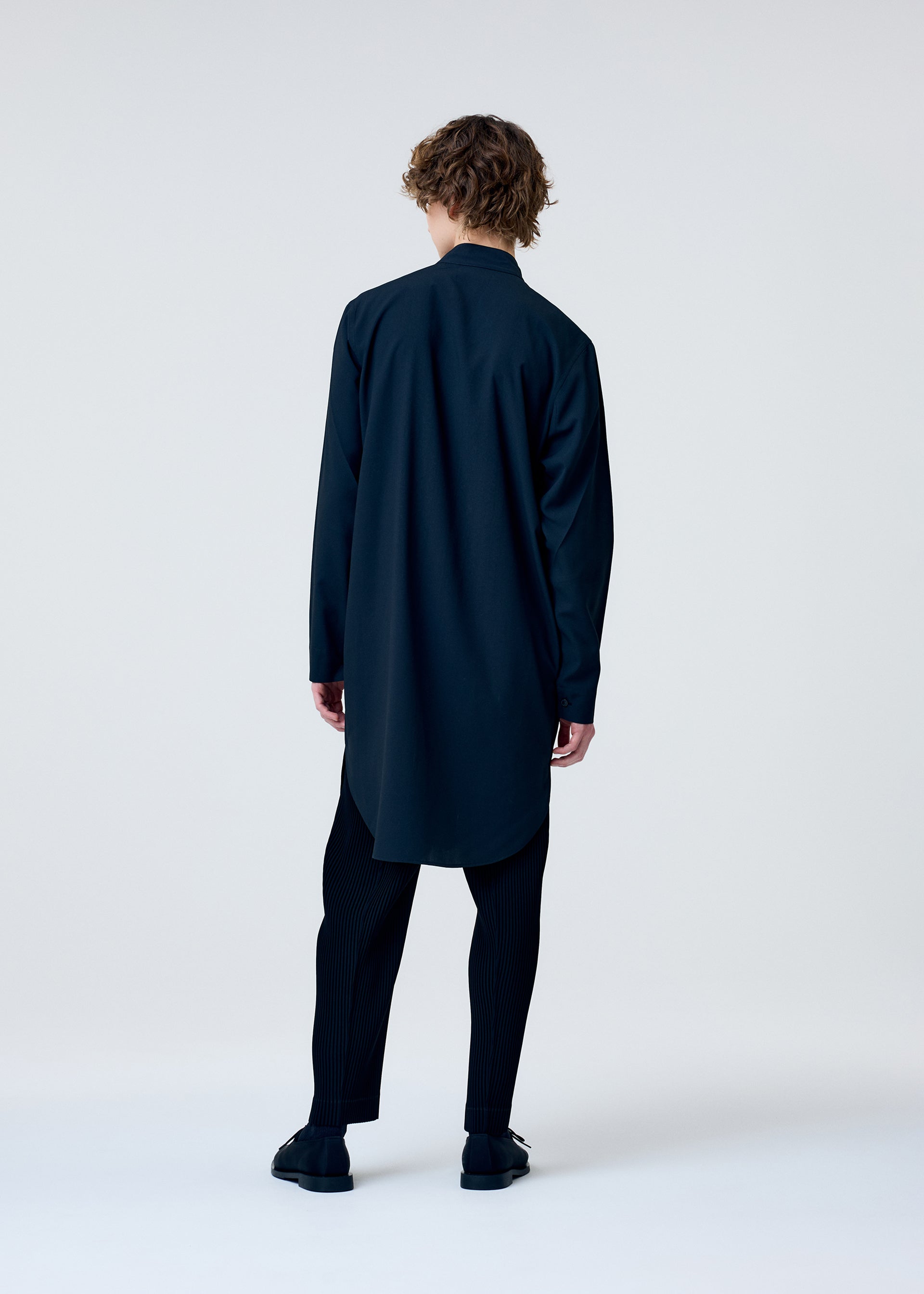 A model wears the HOMME PLISSÉ ISSEY MIYAKE EMBROIDERY PRESS SHIRT shirt.
