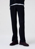 A model wears the HOMME PLISSÉ ISSEY MIYAKE MULTI-FASTENED multi-fastened-trousers-pizza-scorch-brown.
