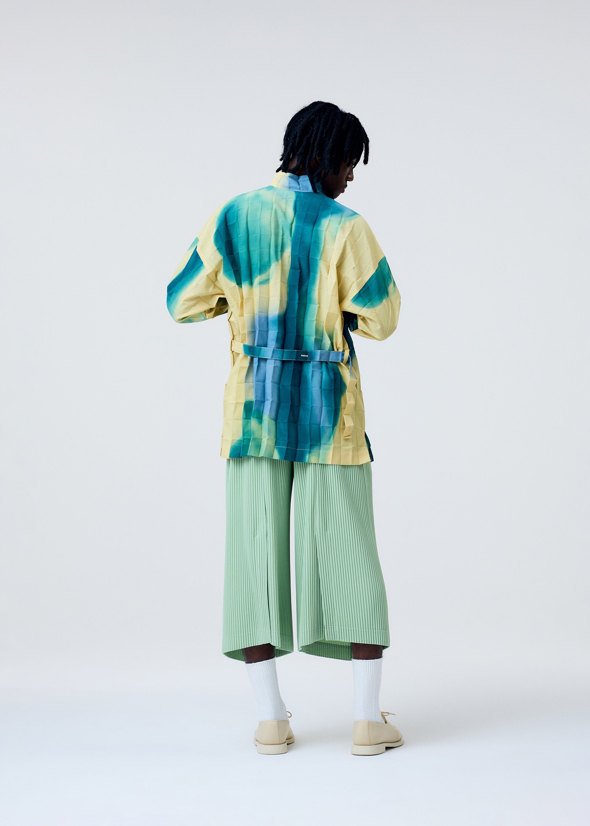A model wears the HOMME PLISSÉ ISSEY MIYAKE PLEATS BOTTOMS 2 trousers.