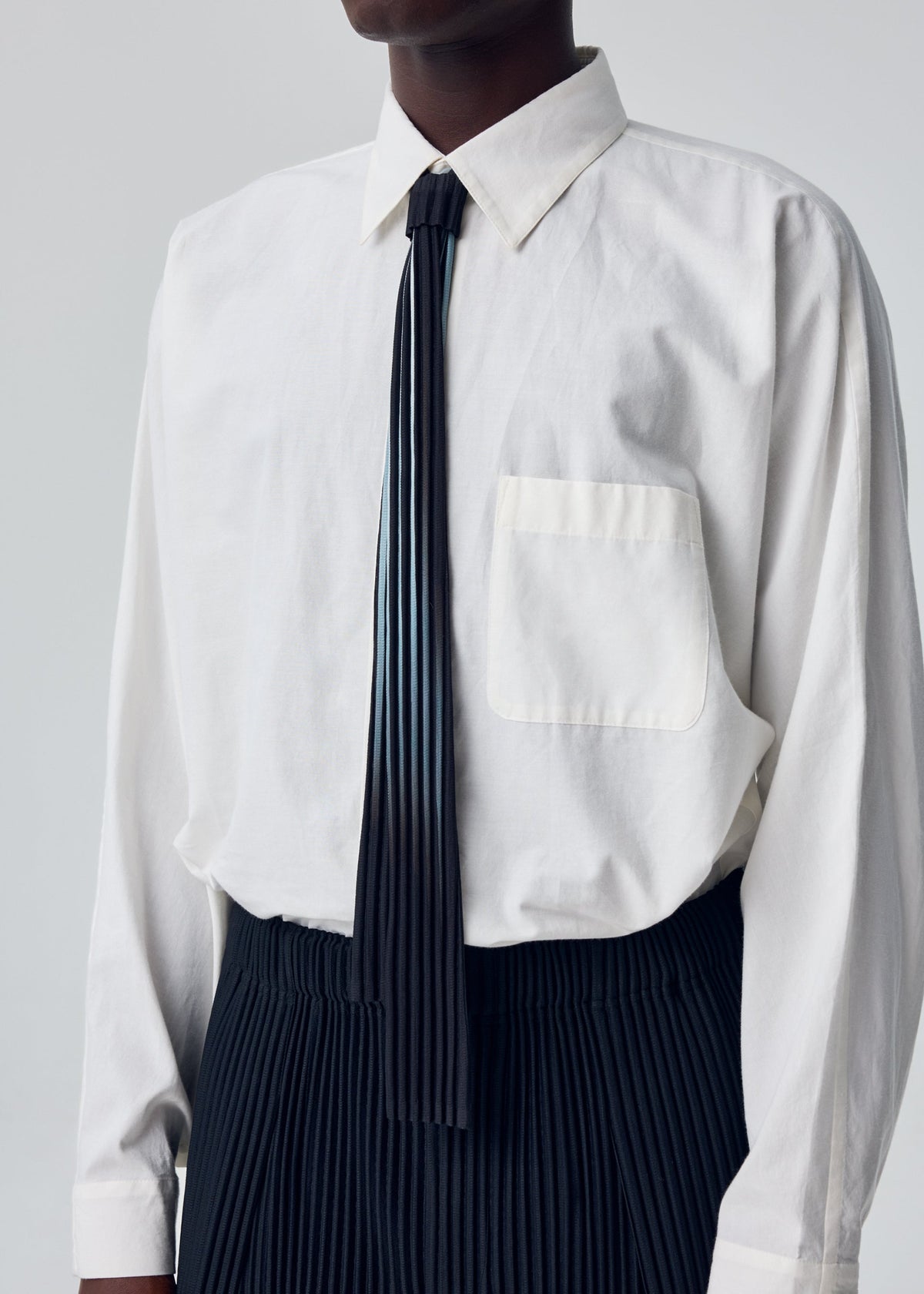 A model wears the HOMME PLISSÉ ISSEY MIYAKE IN THE SHADOW PLEATS TIE in-the-shadow-pleats-tie-tie-shadow-black.