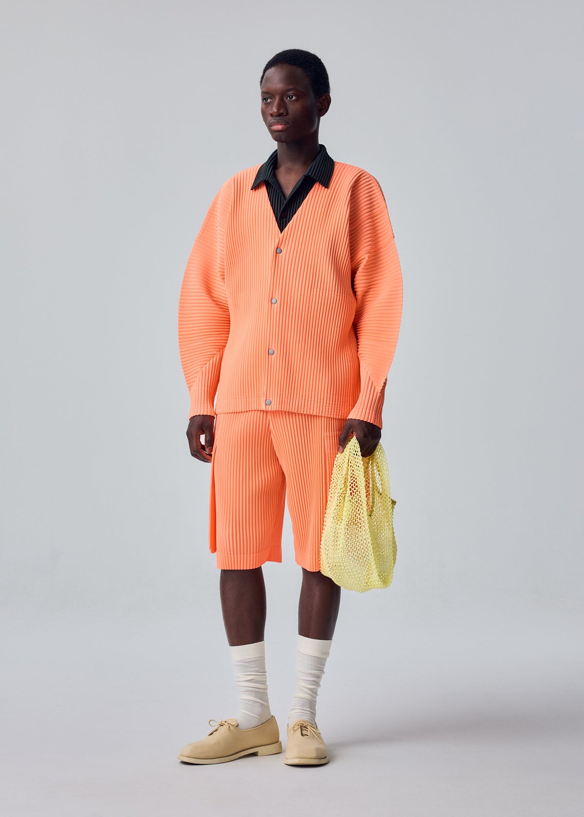 A model wears the HOMME PLISSÉ ISSEY MIYAKE MESH PLEATS BAG mesh-pleats-bag-tote-yellow.