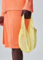 A model wears the HOMME PLISSÉ ISSEY MIYAKE MESH PLEATS BAG mesh-pleats-bag-tote-yellow.