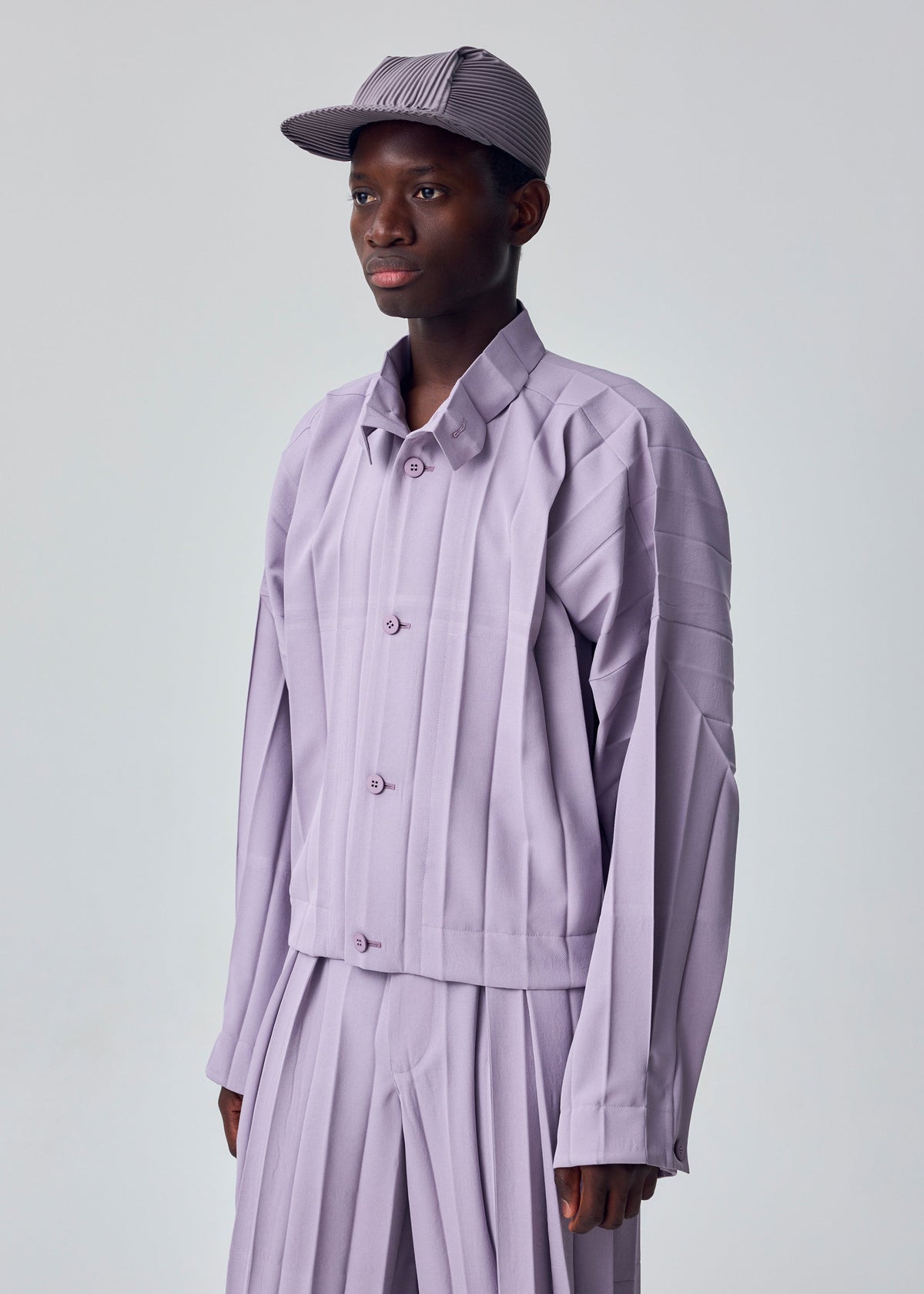 A model wears the HOMME PLISSÉ ISSEY MIYAKE EDGE ENSEMBLE edge-ensemble-jacket-lavender.