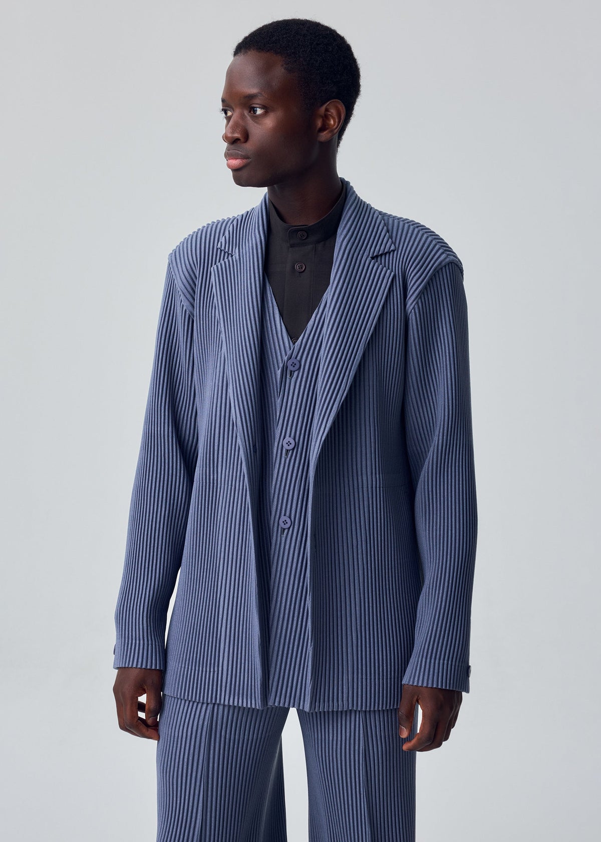 A model wears the HOMME PLISSÉ ISSEY MIYAKE KERSEY PLEATS kersey-pleats-single-breasted-jacket-blue-grey.