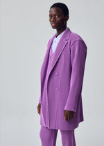 A model wears the HOMME PLISSÉ ISSEY MIYAKE KERSEY PLEATS kersey-pleats-long-jacket-purple.