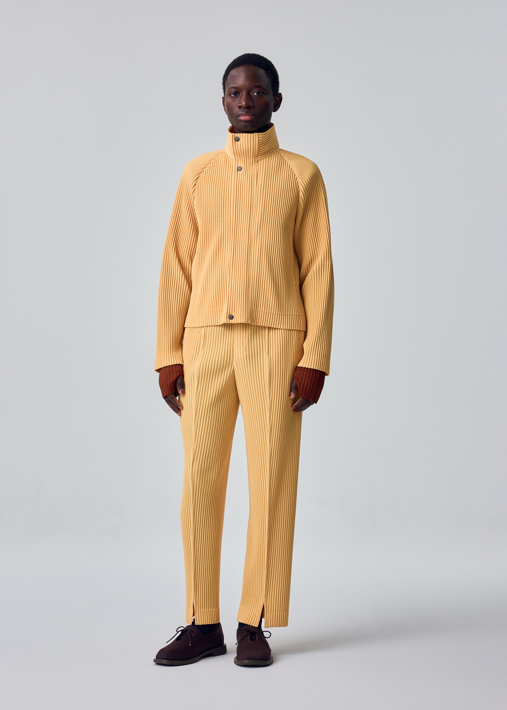 A model wears the HOMME PLISSÉ ISSEY MIYAKE TAILORED PLEATS 1 tailored-pleats-1-raglan-jacket-shadow-brown.
