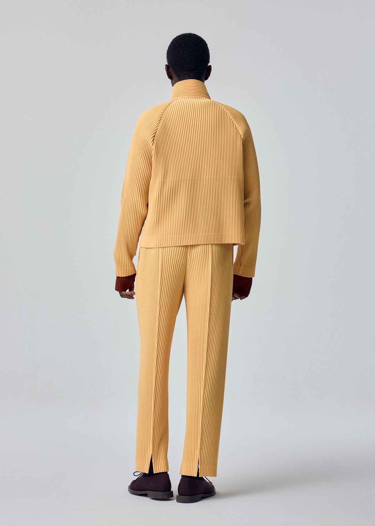 A model wears the HOMME PLISSÉ ISSEY MIYAKE TAILORED PLEATS 1 tailored-pleats-1-raglan-jacket-shadow-brown.