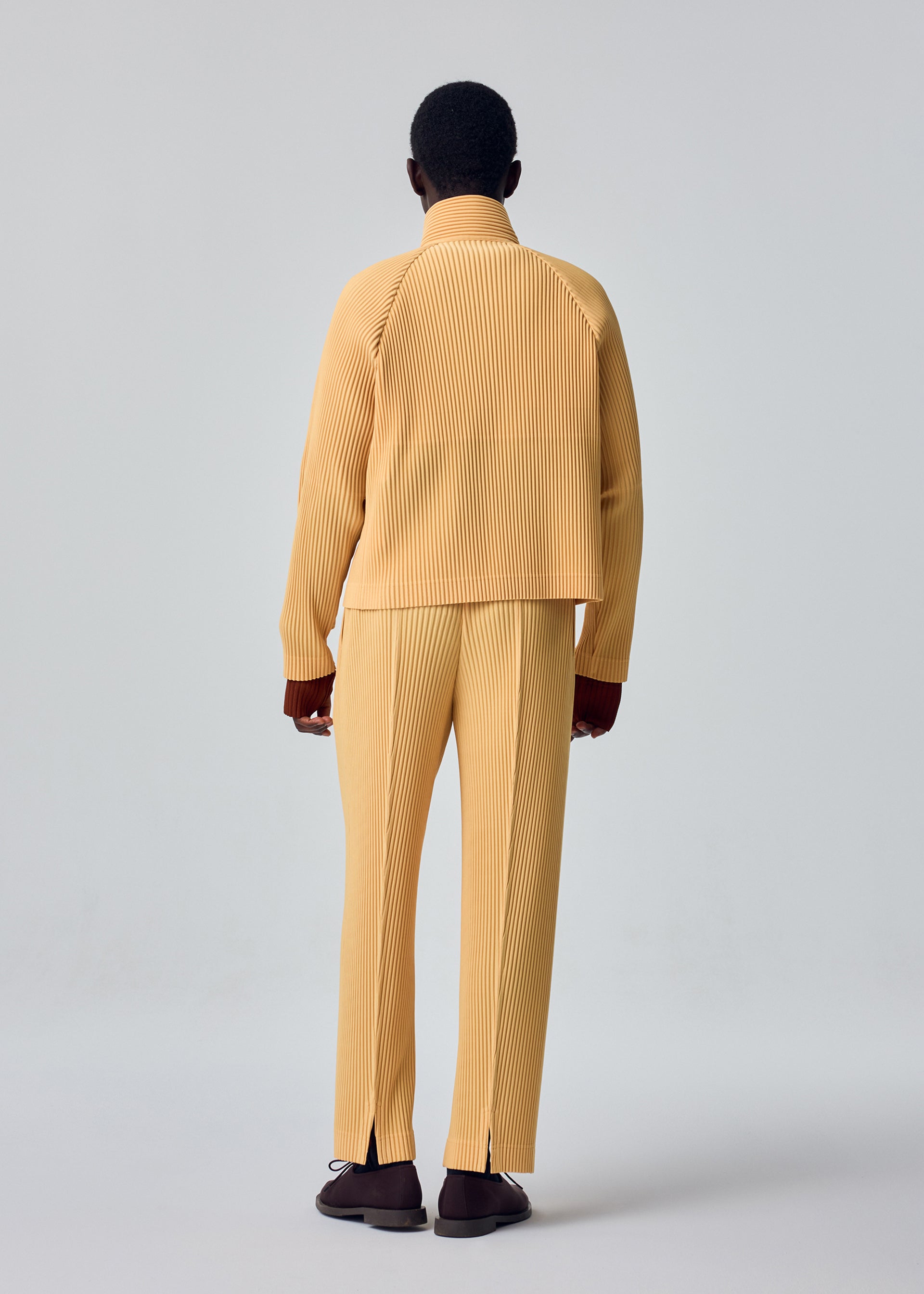 A model wears the HOMME PLISSÉ ISSEY MIYAKE TAILORED PLEATS 1 tailored-pleats-1-raglan-jacket-shadow-brown.