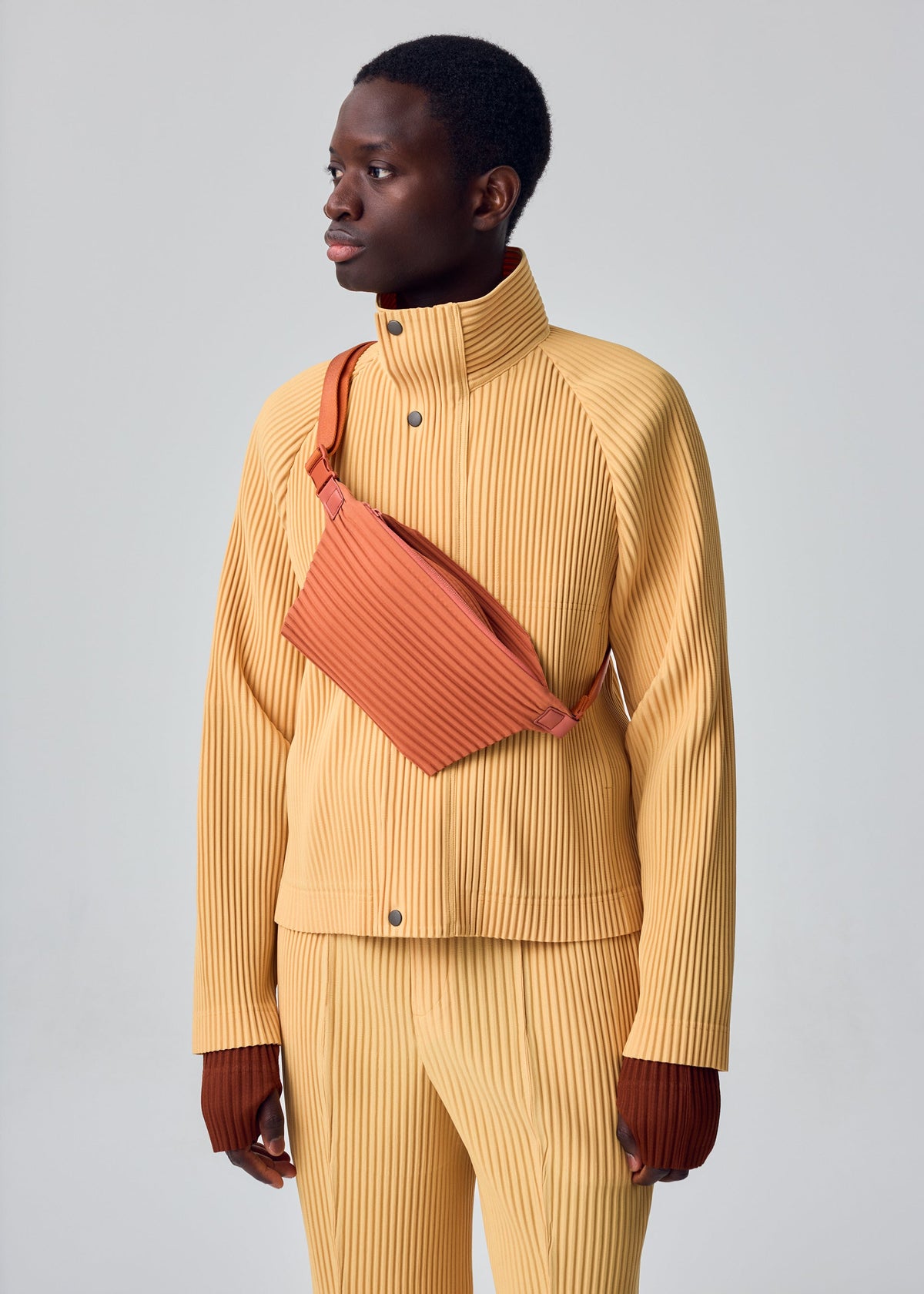 A model wears the HOMME PLISSÉ ISSEY MIYAKE TAILORED PLEATS 1 tailored-pleats-1-raglan-jacket-shadow-brown.