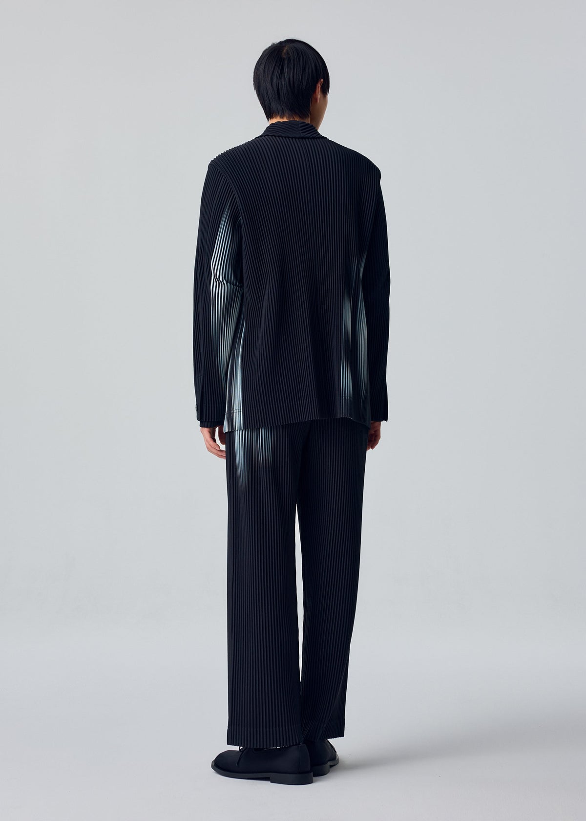 A model wears the HOMME PLISSÉ ISSEY MIYAKE IN THE SHADOW in-the-shadow-jacket-shadow-black.