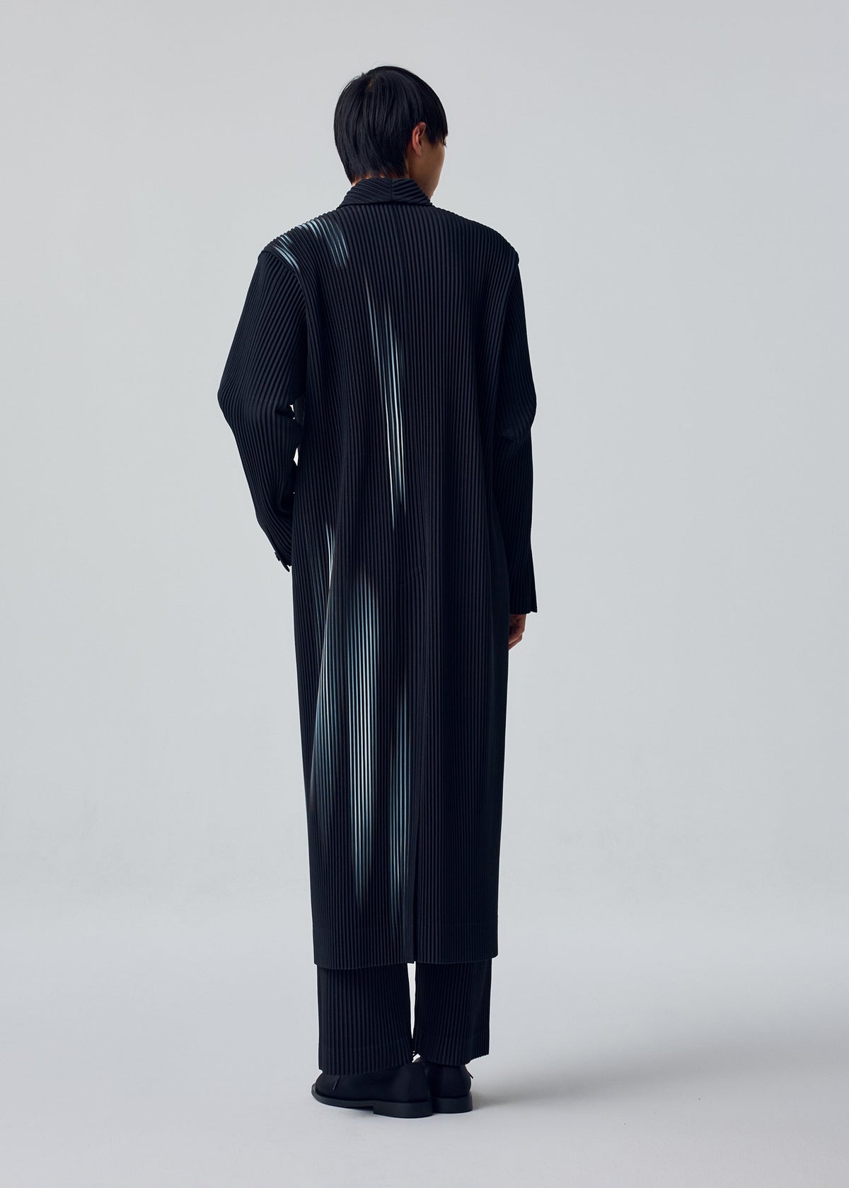A model wears the HOMME PLISSÉ ISSEY MIYAKE IN THE SHADOW in-the-shadow-long-jacket-shadow-black.