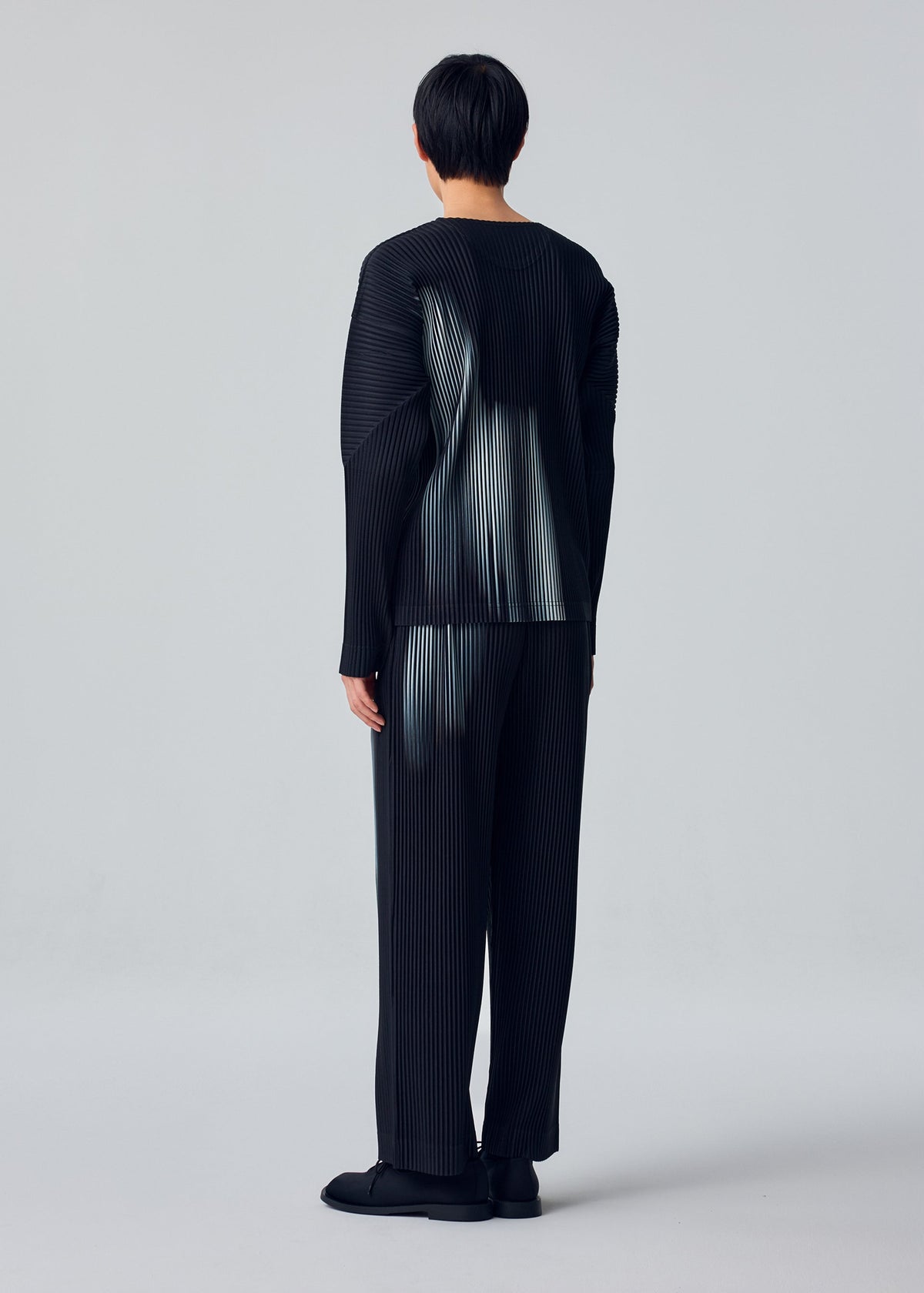 A model wears the HOMME PLISSÉ ISSEY MIYAKE IN THE SHADOW in-the-shadow-trousers-shadow-black.