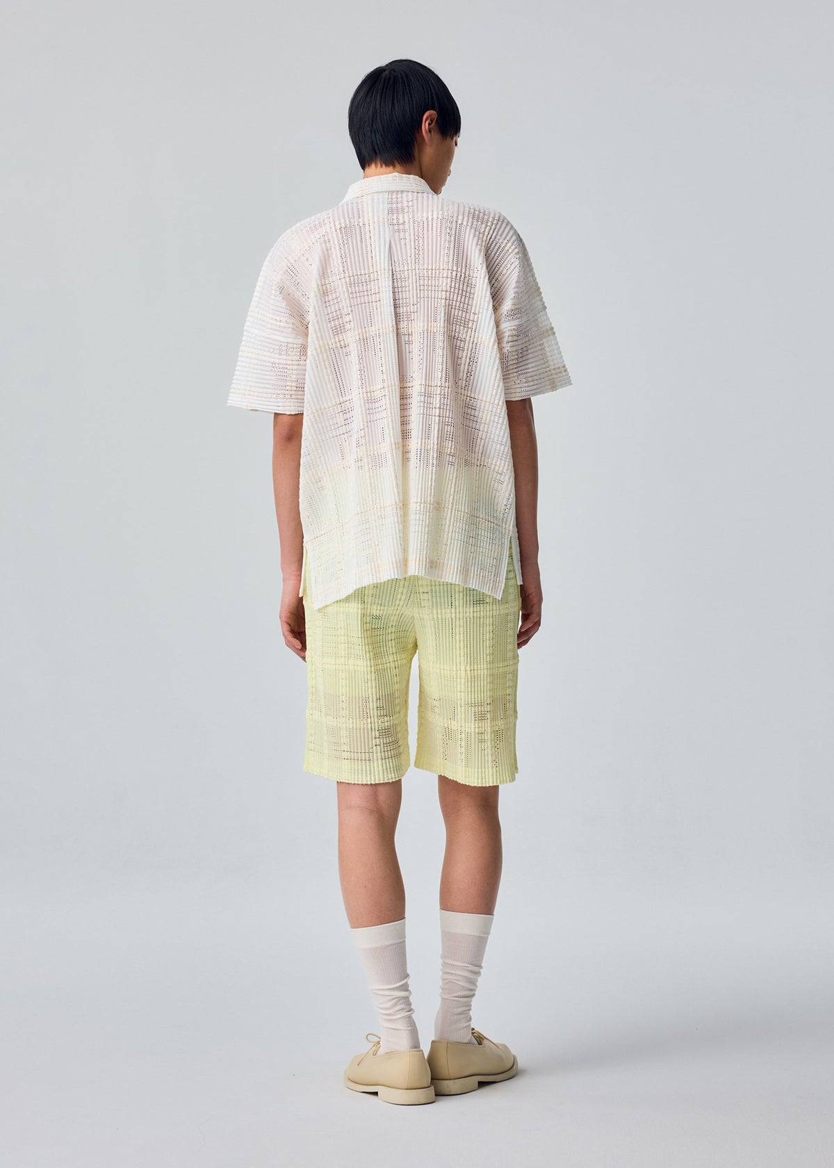 A model wears the HOMME PLISSÉ ISSEY MIYAKE LACE GRID PLEATS lace-grid-pleats-shirt-white.