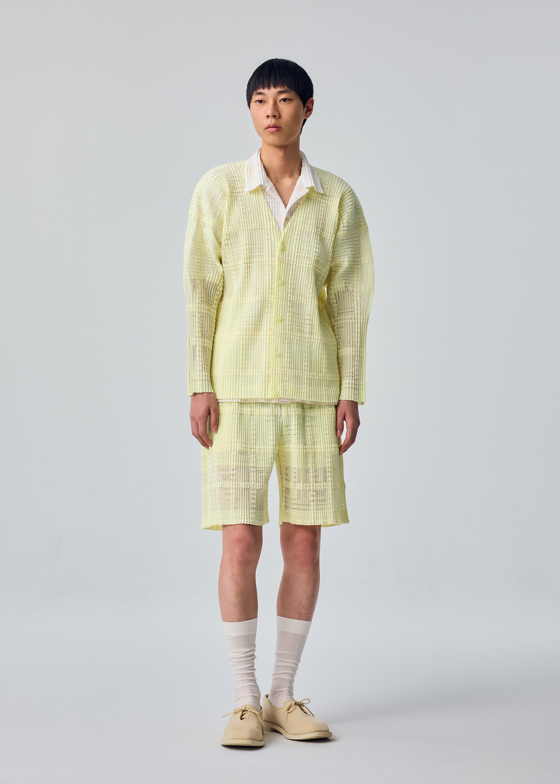 A model wears the HOMME PLISSÉ ISSEY MIYAKE LACE GRID PLEATS lace-grid-pleats-jacket-yellow.