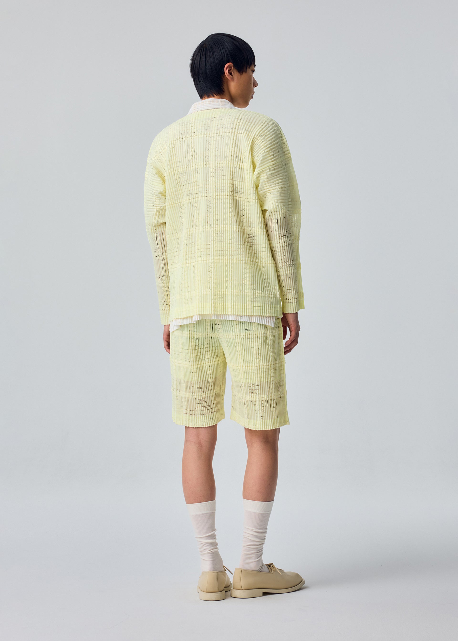 A model wears the HOMME PLISSÉ ISSEY MIYAKE LACE GRID PLEATS lace-grid-pleats-jacket-yellow.