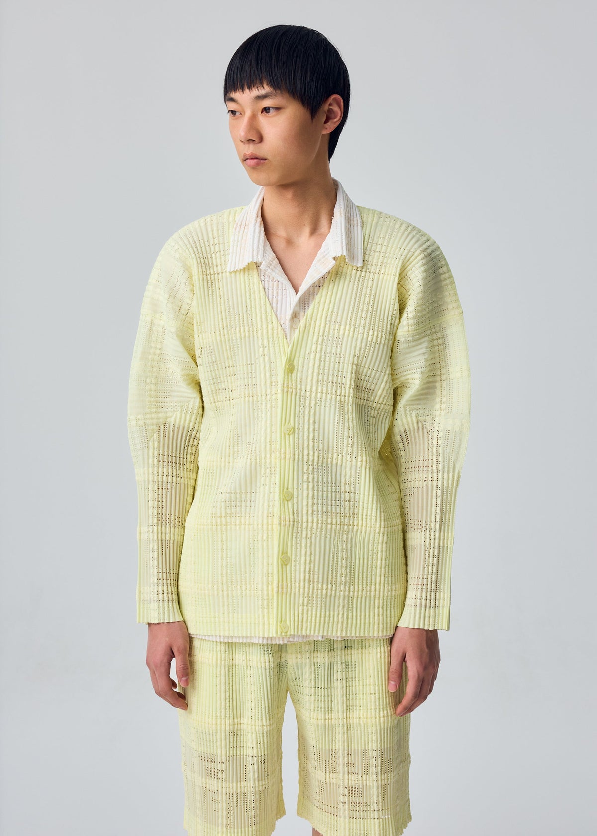 A model wears the HOMME PLISSÉ ISSEY MIYAKE LACE GRID PLEATS lace-grid-pleats-jacket-yellow.