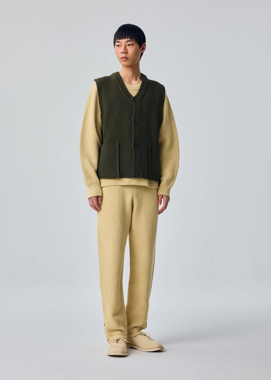 A model wears the HOMME PLISSÉ ISSEY MIYAKE RUSTIC KNIT rustic-knit-vest-yellow-beige.