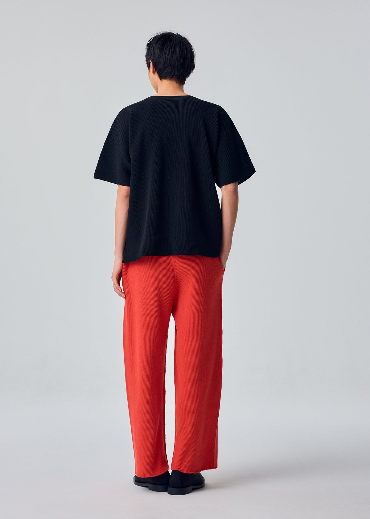 A model wears the HOMME PLISSÉ ISSEY MIYAKE BASIC KNIT basic-knit-t-shirt-top-black.