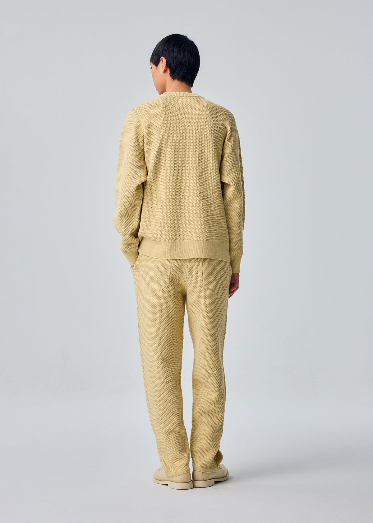 A model wears the HOMME PLISSÉ ISSEY MIYAKE RUSTIC KNIT rustic-knit-top-yellow-beige.