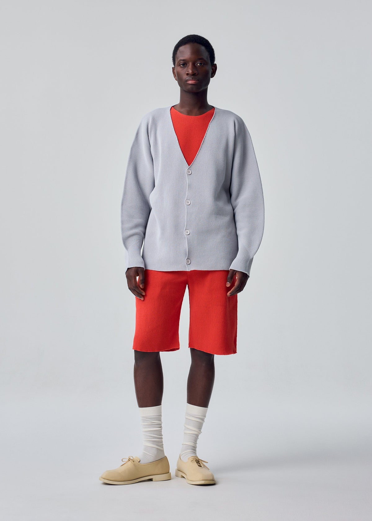 A model wears the HOMME PLISSÉ ISSEY MIYAKE BASIC KNIT basic-knit-button-front-cardigan-black.