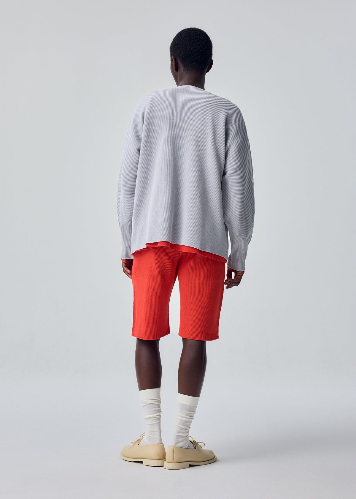 A model wears the HOMME PLISSÉ ISSEY MIYAKE BASIC KNIT basic-knit-button-front-cardigan-black.