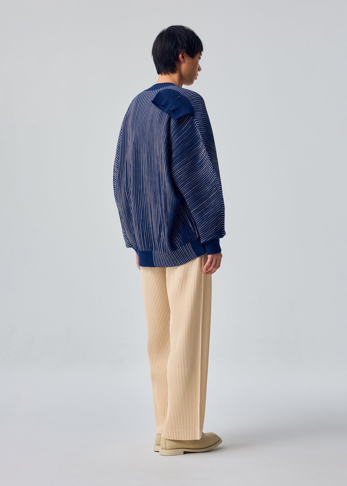 A model wears the HOMME PLISSÉ ISSEY MIYAKE IN THE SHADOW KNIT in-the-shadow-knit-cardigan-black.