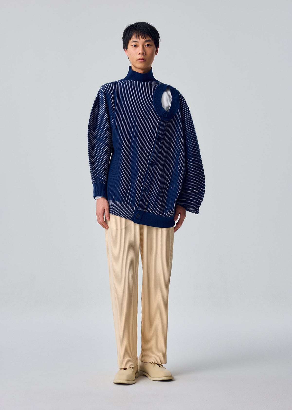 A model wears the HOMME PLISSÉ ISSEY MIYAKE IN THE SHADOW KNIT in-the-shadow-knit-cardigan-blue.