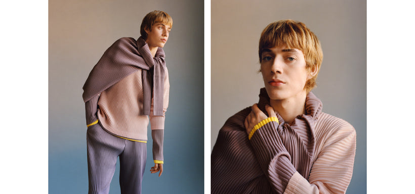 Left: Model wearing COLOR PLEATS Top in Seaside Purple and PLEATS BOTTOMS 1 Trousers in Burnt Purple, with COLOR PLEATS Top in Edge Browns wrapped around the neck, posed in a relaxed stance against a gradient beige and blue background. Right: Model wearing COLOR PLEATS Top in Seaside Purple, with COLOR PLEATS Top in Edge Browns wrapped around the neck, looking straight at the camera. Set against a gradient beige and blue background.