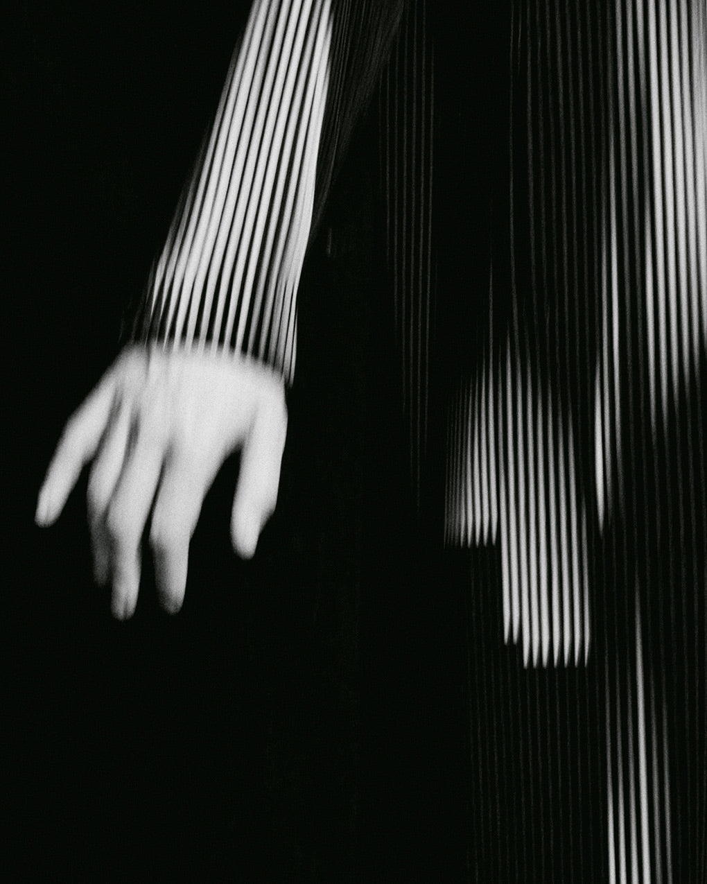 Black and white closeup of model wearing black and white printed pleated long coat. Posing against a black background.