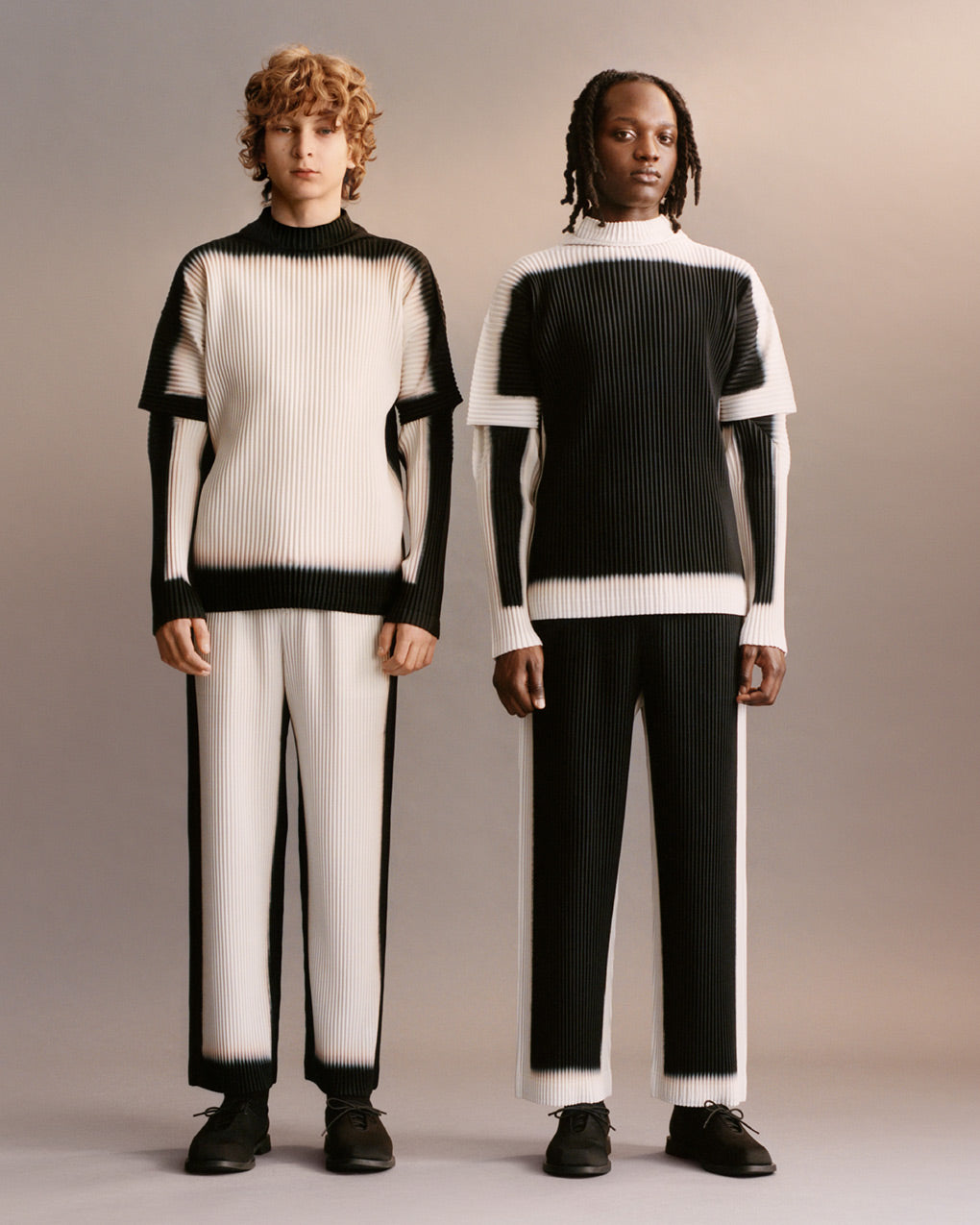 Two models standing next to each other wearing the inverse versions of a black and white printed pleated set with black shoes. Posing in front of a light grey background.