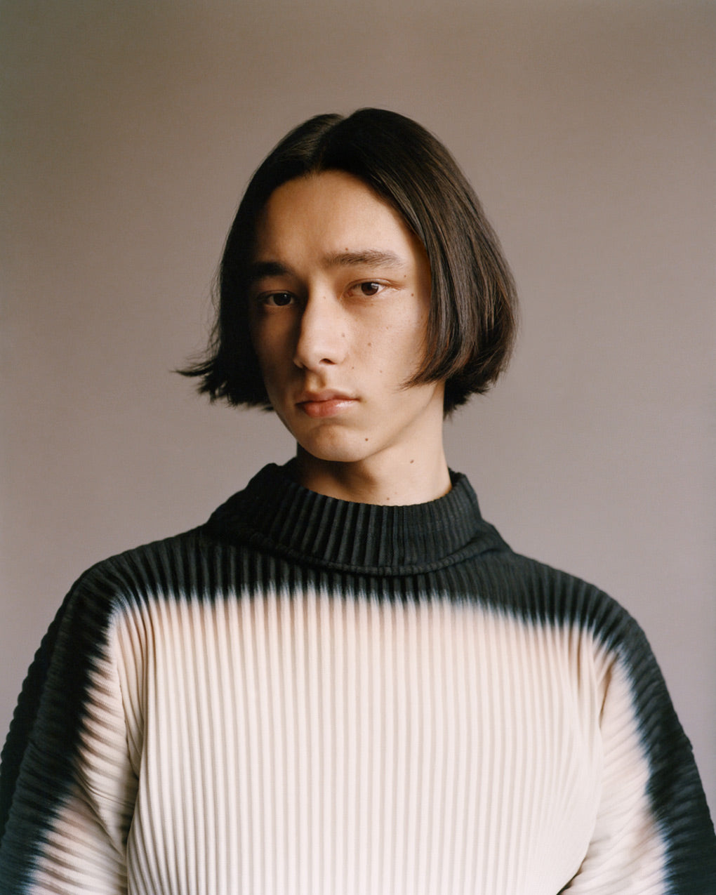 Portrait of a model wearing a black and white turtleneck top. Posed in front of a light grey background.