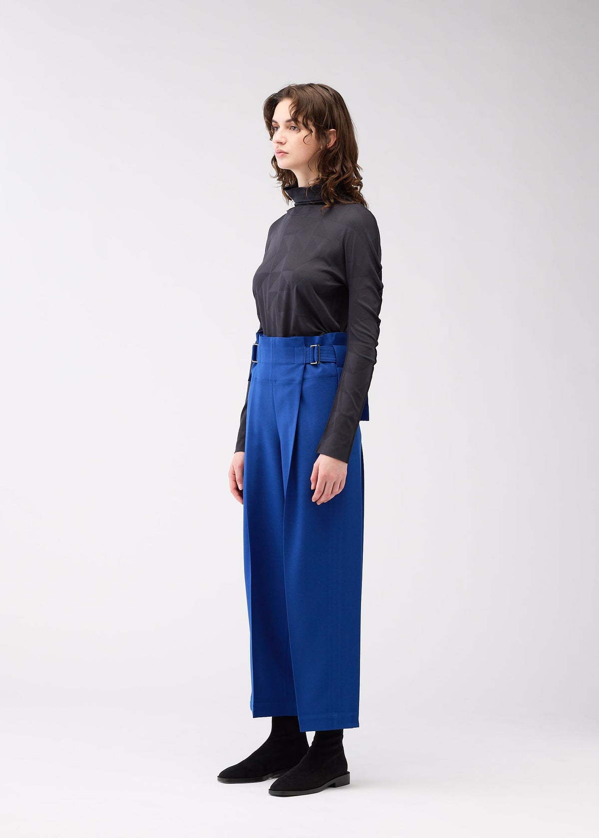 A model wears the 132 5. ISSEY MIYAKE WOOL LIKE FLAT TUCK trousers.