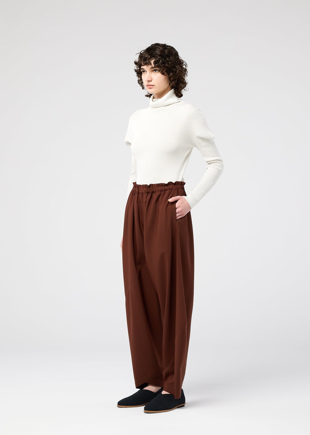 A model wears the 132 5. ISSEY MIYAKE PARALLEL WRAP trousers.