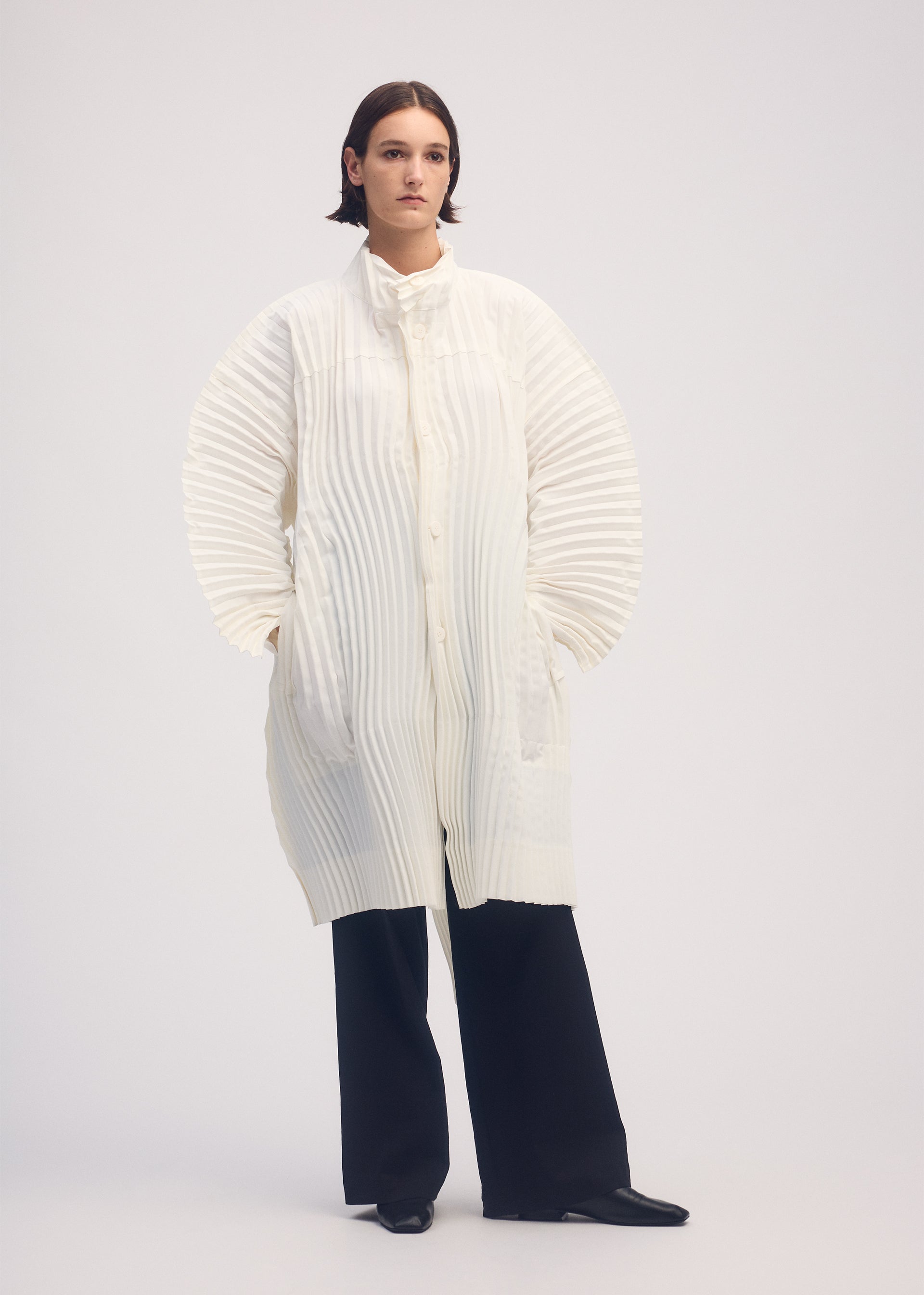 A model wears the ISSEY MIYAKE WAVERING PLEATS coat.