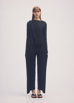 A model wears the ISSEY MIYAKE SHADOW STUDY PLEATS SOLID trousers.