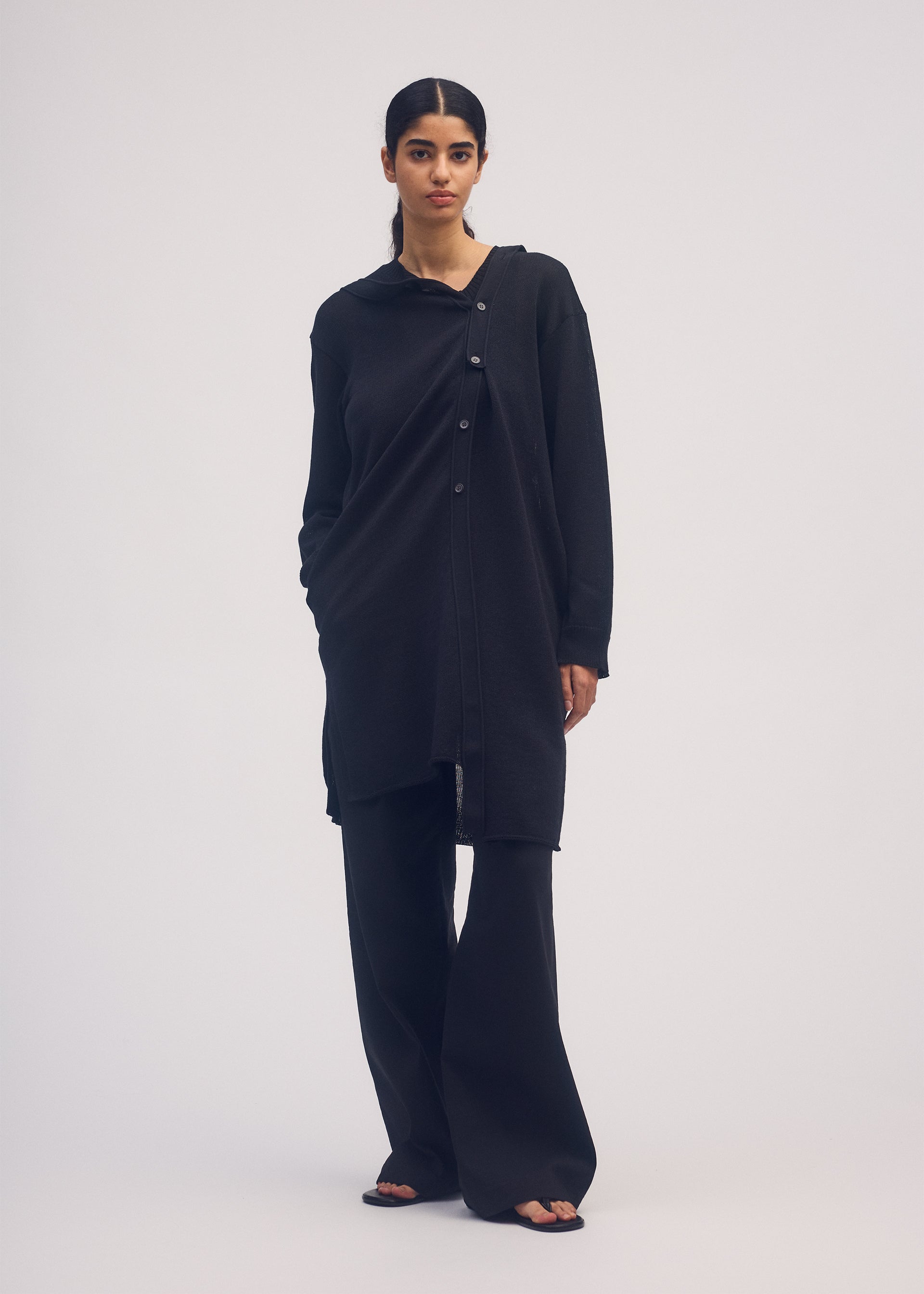 A model wears the ISSEY MIYAKE BUTTONED DRAPE KNIT cardigan.