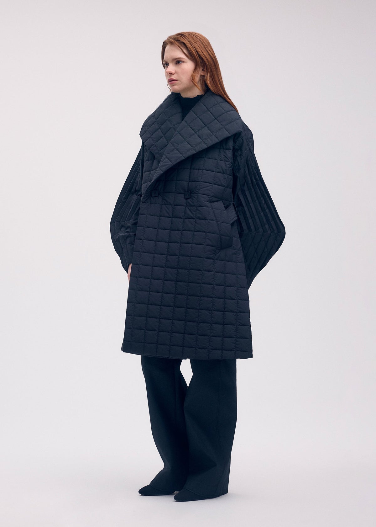 A model wears the ISSEY MIYAKE PLEATED GRID coat.