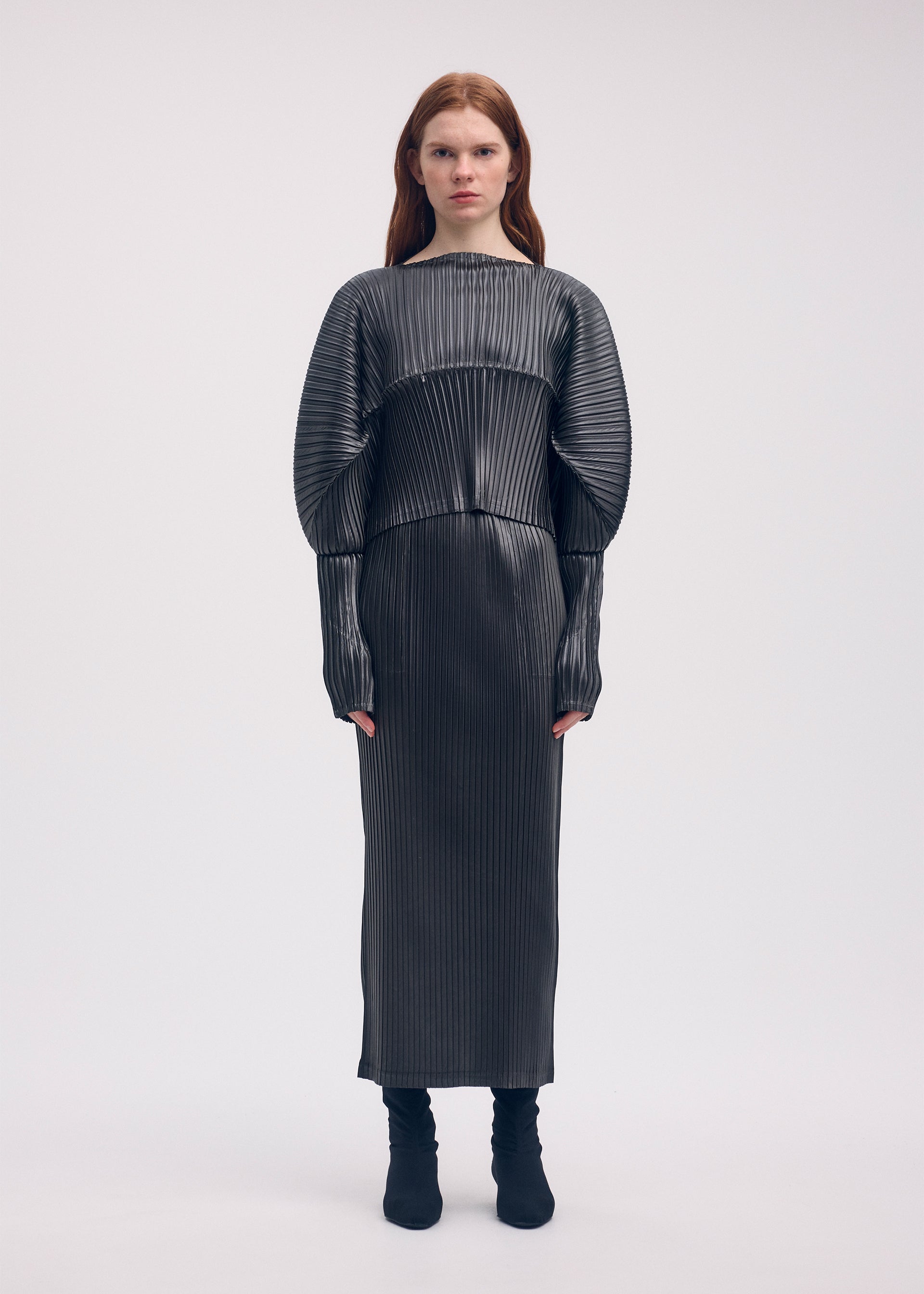 A model wears the ISSEY MIYAKE GLOSSED METAL PLEATS skirt.