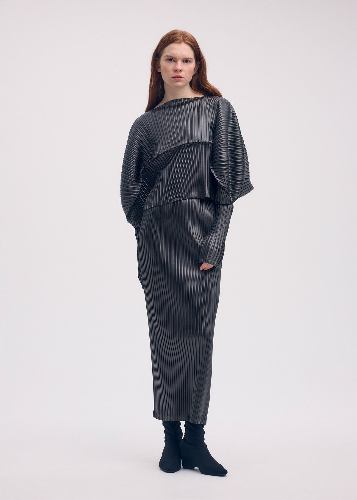 A model wears the ISSEY MIYAKE GLOSSED METAL PLEATS skirt.