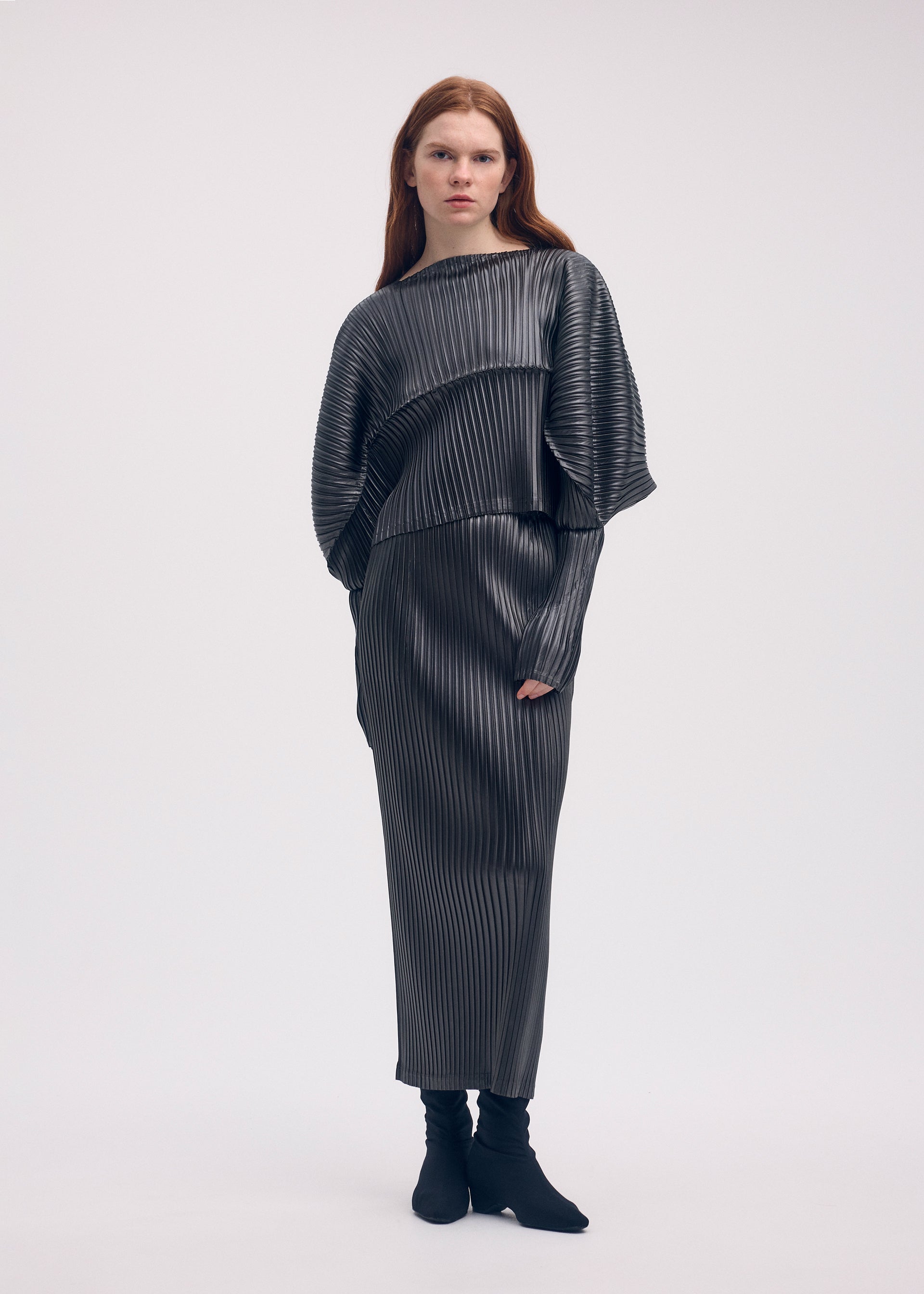 A model wears the ISSEY MIYAKE GLOSSED METAL PLEATS skirt.