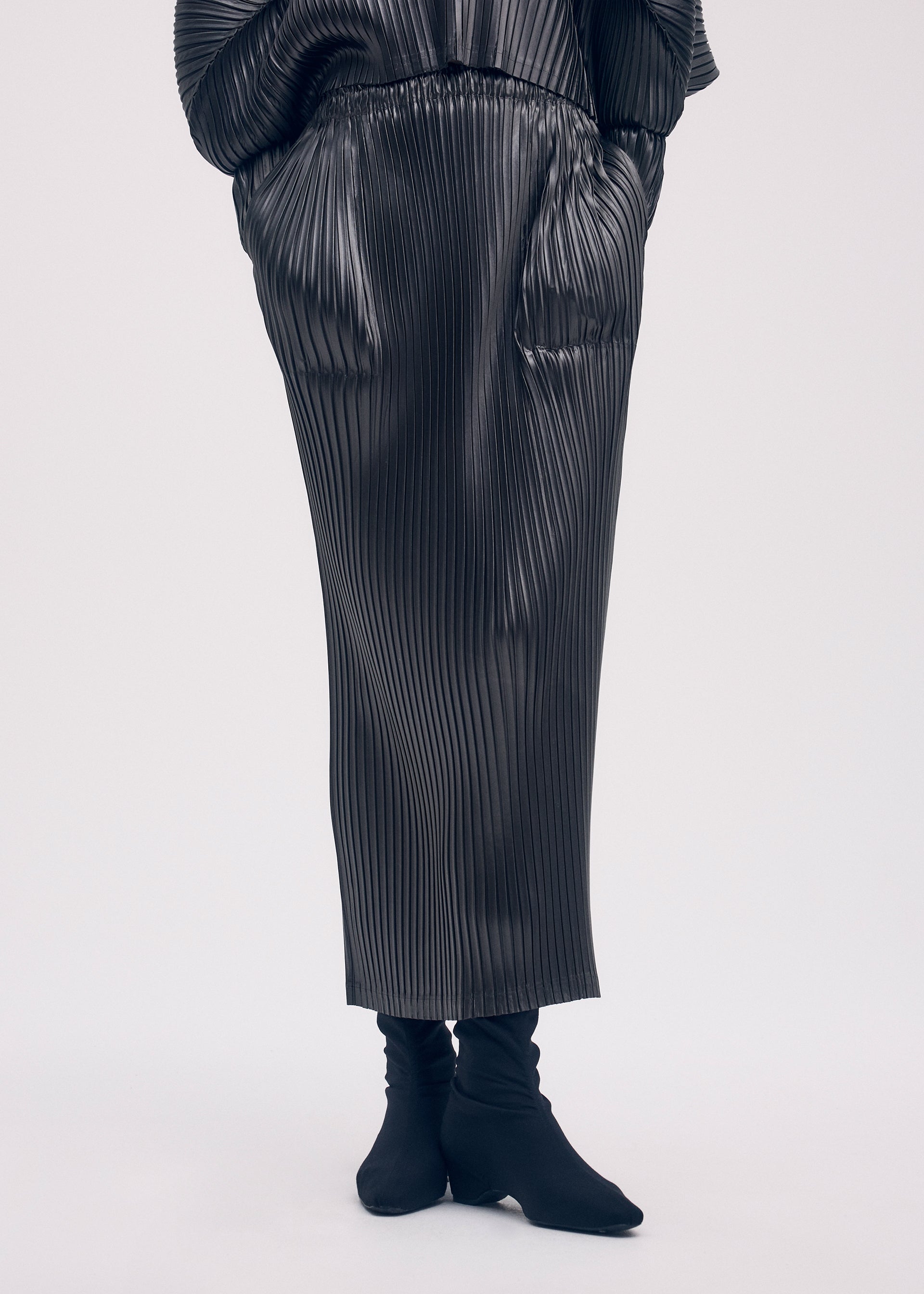 A model wears the ISSEY MIYAKE GLOSSED METAL PLEATS skirt.
