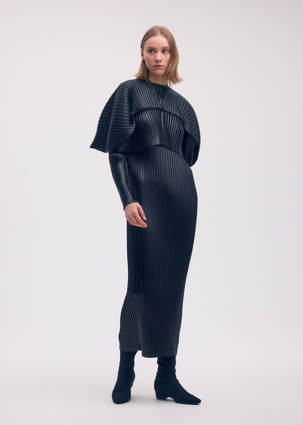 A model wears the ISSEY MIYAKE GLOSSED METAL PLEATS cardigan.