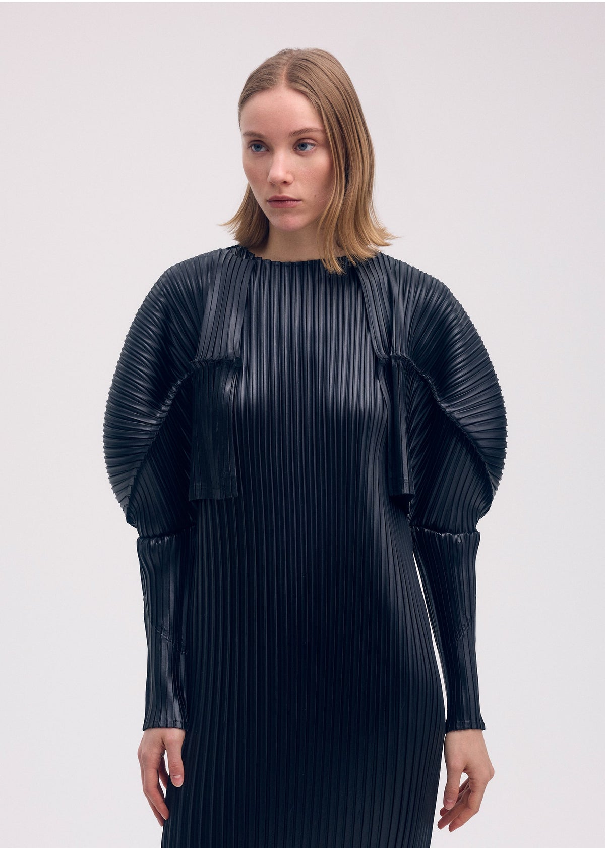 A model wears the ISSEY MIYAKE GLOSSED METAL PLEATS cardigan.