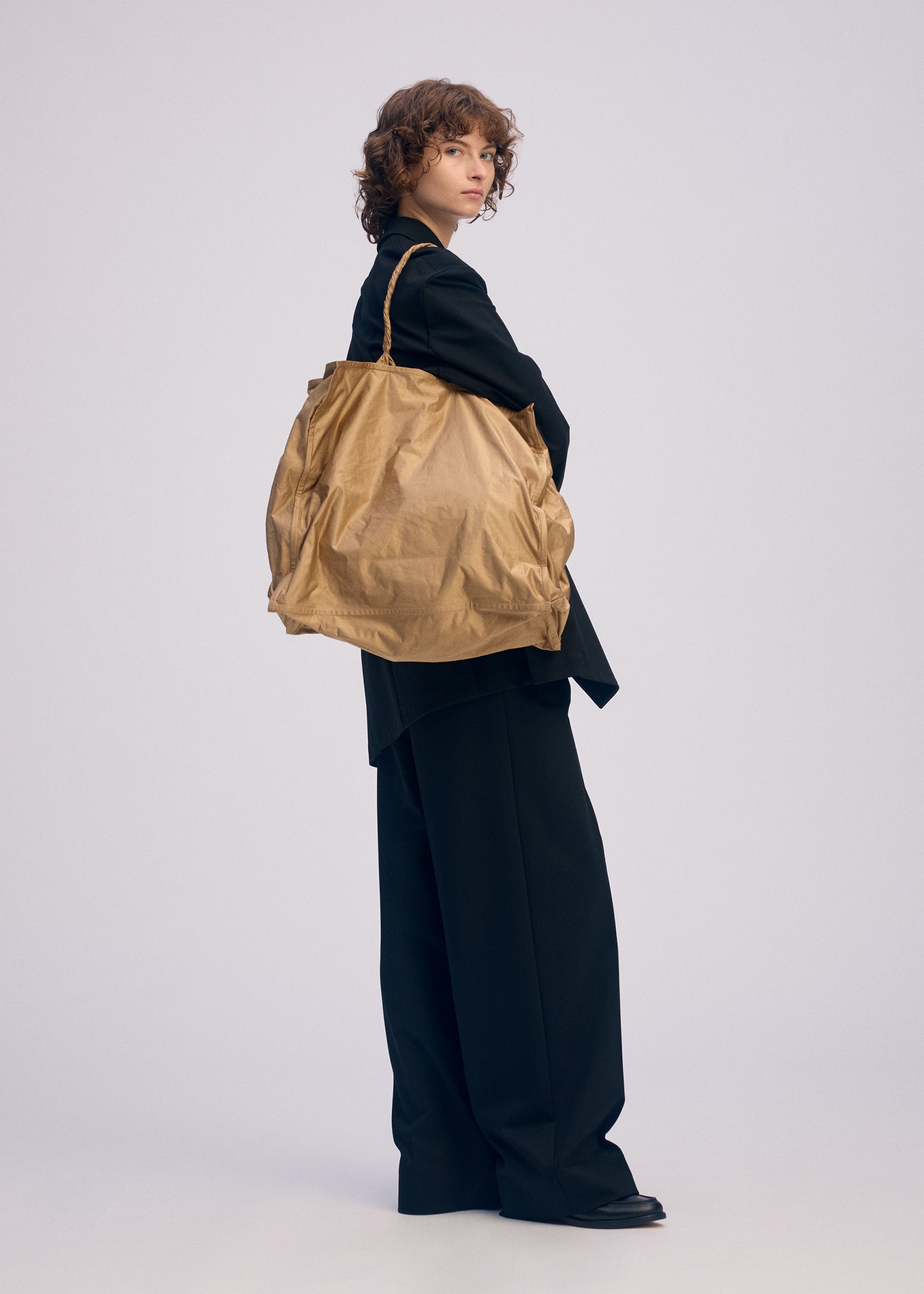 A model wears the ISSEY MIYAKE CRUMPLABLE bag.